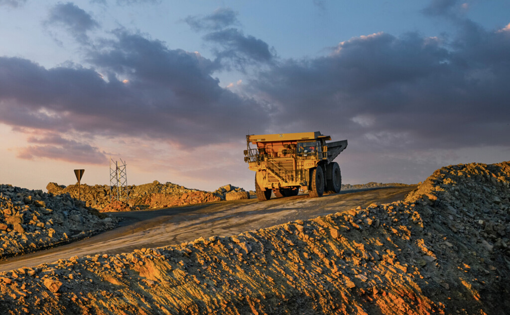 Large mining dump truck on a dirt road at sunset, with rocky piles surrounding the site.
