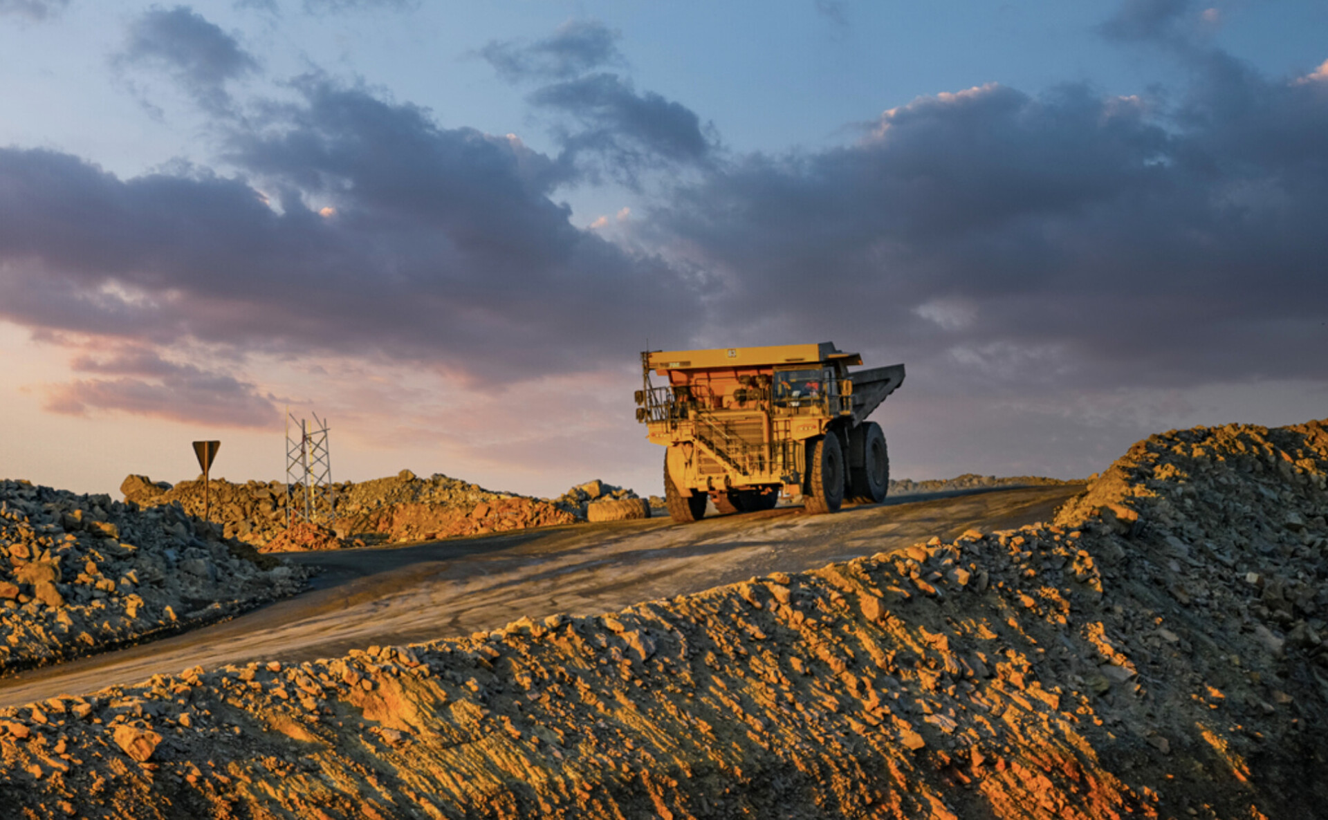 Large mining dump truck on a dirt road at sunset, with rocky piles surrounding the site.